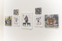 The gallery wall displays five artworks by Steve Seeley, with three larger frames featuring acrylic figures and animals with gold leaf, and two smaller ones showing abstract designs. All pieces are evenly spaced on a light-colored wall.