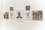 A gallery wall showcases Steve Seeleys framed art pieces of yokai, people, animals, and abstract designs. Two smaller black and white patterned canvases add intrigue above on a plain white wall.