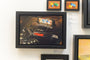 Allan Innman offers a framed artwork of a Sega Genesis console and controller with a Sonic game cartridge, resembling an exhibit at Spoke Art Gallery, surrounded by smaller frames featuring colorful Lego bricks.