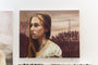 A Michael Ramstead oil on canvas features a woman with long brown hair, a white blouse, and turquoise necklace. She gazes sideways against a backdrop of trees and cloudy sky, while birds rest on power lines in the distance, echoing styles seen at Spoke Art Gallery.