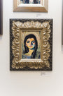 A Rich Pellegrino painting of a woman with vibrant facial features, created in acrylic on board, is showcased in an ornate carved frame on a white wall among other artworks. A small label with the price is displayed beneath it.