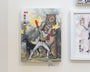 Steve Seeleys acrylic painting Peace Makers features a superhero in gray and red armor with arms raised, standing with a bear and dog among yellow birds. Adorned with gold leaf accents, its displayed on a white wall among other framed artworks.