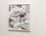 A framed Jonas Lofgren graphite drawing of a living room with a sofa, round table, plants, and abstract art adorns The Attics white gallery wall.