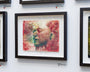 The Akira Beard framed watercolor artwork showcases a serene side profile with ink text and vibrant red and green splashes, creating an abstract effect. Its displayed on a white wall alongside other pieces.