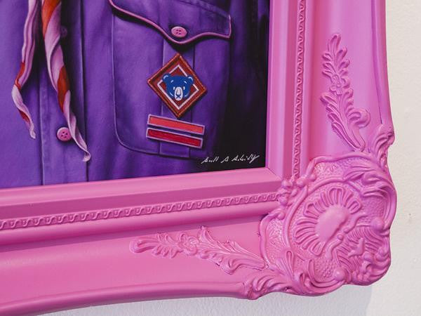 Close-up of a vivid pink ornate frame containing a painting of a purple uniform adorned with badges and a striped scarf. This limited edition by Scott Scheidly features intricate floral designs and includes his signature.