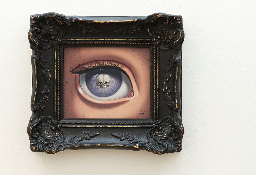 An ornately framed painting by Ana Bagayan, depicts a skeleton eye with a purple iris featuring a tiny skull. The dark, intricate frame complements the artworks mysterious theme perfectly.