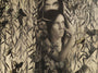 An Alessandra Maria grayscale painting depicts a woman with her sister among foliage and flowers, butterflies with subtle yellow highlights resembling delicate gold leaf fluttering around. The womans contemplative expression is framed by another face above, partially obscured by leaves.