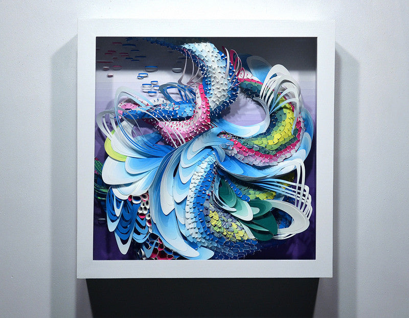 Crystal Wagners vibrant abstract art showcases layered swirling shapes in blue, pink, green, and white. The textured design resembles waves or feathers and is framed in a white square frame on a wall, reflecting cut paper techniques.