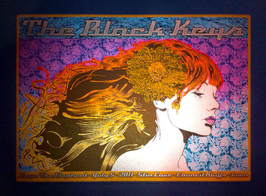 A custom-framed Chuck Sperry poster showcases a womans profile with red and gold hair against a patterned backdrop. It features The Black Keys concert details with Cage the Elephant, dated July 6, 2011, at Stir Cove, Council Bluffs, Iowa.