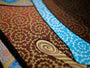 Close-up of an intricate, colorful abstract design with swirling blue and white lines on a brown and gold background, resembling a dynamic Chuck Sperry limited edition screen print.