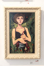 Kelsey Becketts framed acrylic painting, Sur Le Fil, features a woman with short brown hair in a black dress with white polka dots, holding a fish surrounded by greenery and red berries. It is in an ornate light frame.