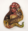 Vivid oil on birch by Tatiana Suarez features a fantastical figure with colorful hair, bold makeup, and a margay. Grapes and swirling hues amplify its ethereal and magical vibe.