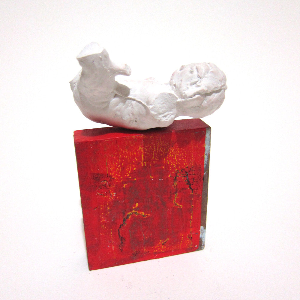 A white abstract plaster sculpture of a seated figure by Tessar Lo is elegantly mounted on a textured red and orange rectangular base, shining beautifully against the plain white background.
