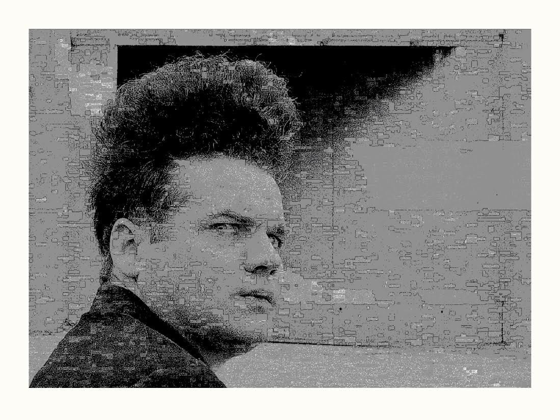 A man with dark, tall, and voluminous hair reminiscent of Henry Spencer intently stares sideways. The gritty overlay, similar to an Eraserhead screen print, adds a vintage touch. The plain wall accentuates his expression in this artistic portrait from the Tim Jordan brand.