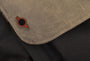 Close-up of a brown fabric flap adorned with an embossed metal pin featuring a black and red circular emblem. The flap rests on black textured material, part of a Joel Daniel Phillips Red Rising-themed bag or backpack.
