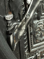 Close-up of a textured sculpture by Handiedan, showcasing a figure with a sword. A bubble asks, WHAT IS SHE DOING HERE, BUDDY? WHO IS SHE? The piece features intricate patterns and geometric shapes, reminiscent of Counterfeiter No.4.