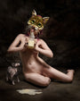 In a dim room with a textured backdrop, someone kneels wearing a cat mask and drinks milk as a small hairless cat watches. This intriguing scene echoes surreal moments from Ransom & Mitchells exclusive posters for the Lil Bub Art Exhibit.
