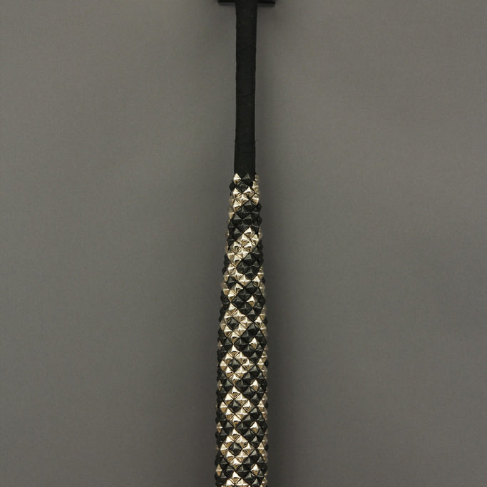 A baseball bat featuring black and white crystals and metallic spikes stands upright against a gray background. The patterns on the handle create a unique visual effect, echoing Lucien Shapiros mixed media artistry.