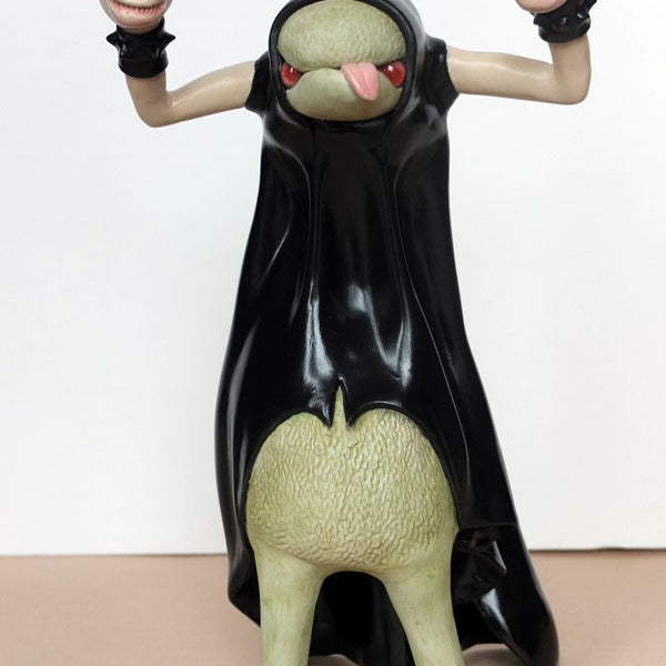 A green creature with a large belly and a black cloak, sculpted by Doubleparlour from resin, sticks its tongue out. It has two raised arms ending in mask-like faces and stands on two legs with black shoes, detailed with acrylic paint.