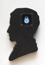 A hand-cut wood plaque by Matt Ritchie features a persons silhouette with an acrylic painting inside, depicting a cartoonish blue padlock icon in a square frame.