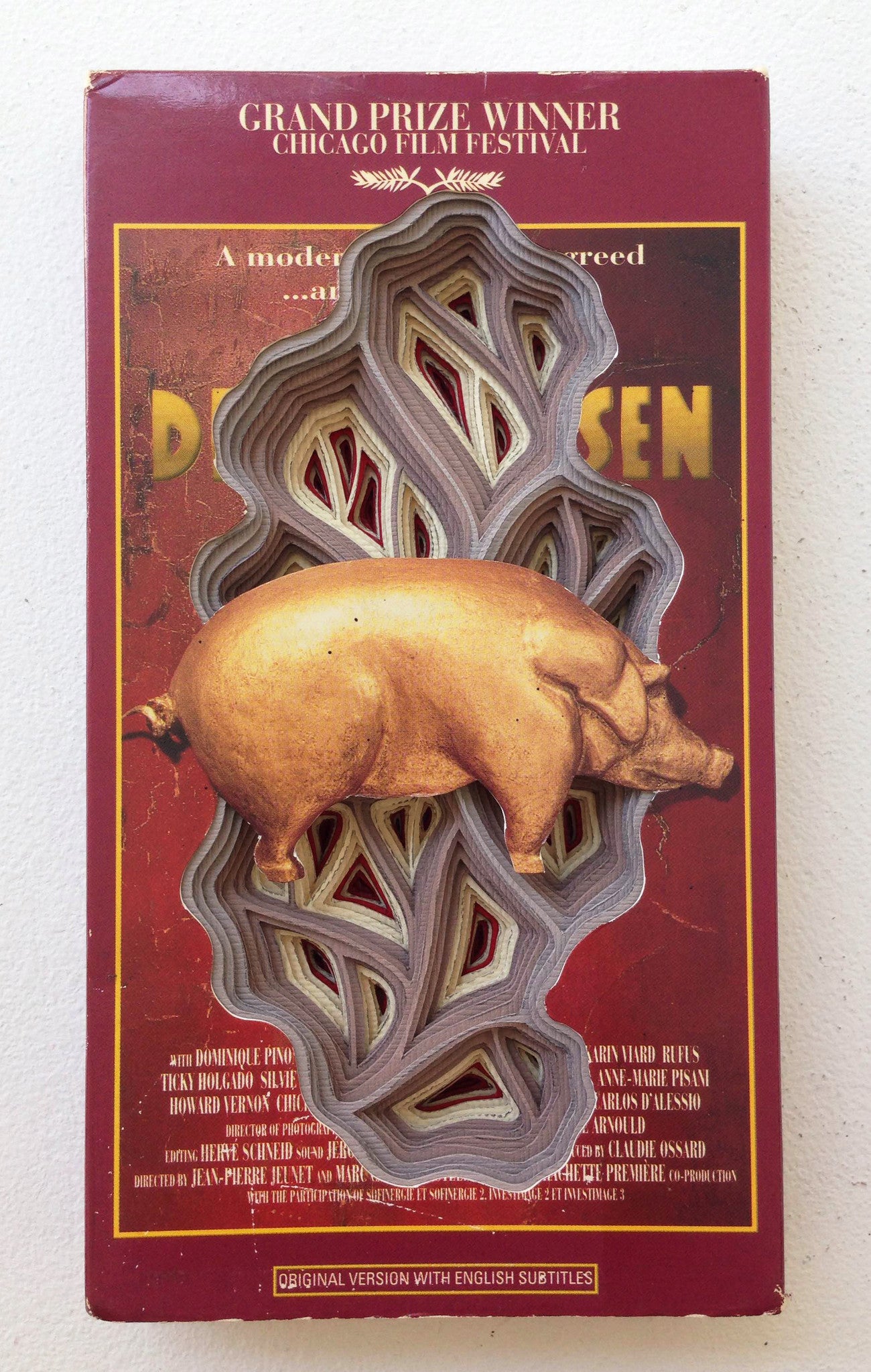A hand-cut, layered book by Charles Clary unveils a pig sculpture inside. The cover highlights text about a Chicago Film Festival grand prize winner, while the pig is set against a burgundy backdrop with partially visible text.