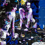 A vibrant collage on canvas by Derek Gores features abstract female figures in purple and white, surrounded by text fragments and magazine cutouts. The dark-hued background with random graphics creates a chaotic atmosphere ideal for any art gallery.