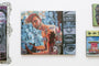 A vibrant painting by Serge Gay Jr. features a shirtless person among mannequins, acrylic on canvas. The artwork includes abstract shapes, a wine glass, and face close-ups to the right, exhibited at Spoke Art Gallery.