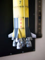 Close-up of a Steve Yamane yellow and gray model rocket with USA vertically, echoing Kubricks detailed style. The model showcases multiple thrusters at its base, reminiscent of Room 237s mystery, set against a dark background.