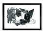 Joel Phillipss fine art giclée print features a black and white image of a person sitting on the ground reading beside a shopping cart full of belongings and a makeshift shelter made of sheets and poles. Elegantly framed in black, this piece captures the scene with stunning detail.