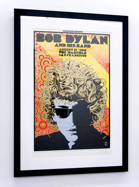 This custom framed print by Chuck Sperry showcases a psychedelic Bob Dylan concert art, featuring a stylized man with curly hair and sunglasses against a vibrant background. It includes concert details from August 25, 2010, in San Francisco.