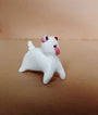 Doubleparlours charming white ceramic figurine, Little Bashlu, showcases a spiral-tailed dog with red eyes and a playful tongue against a beige backdrop, highlighting the allure of hand-sculpted resin artistry.