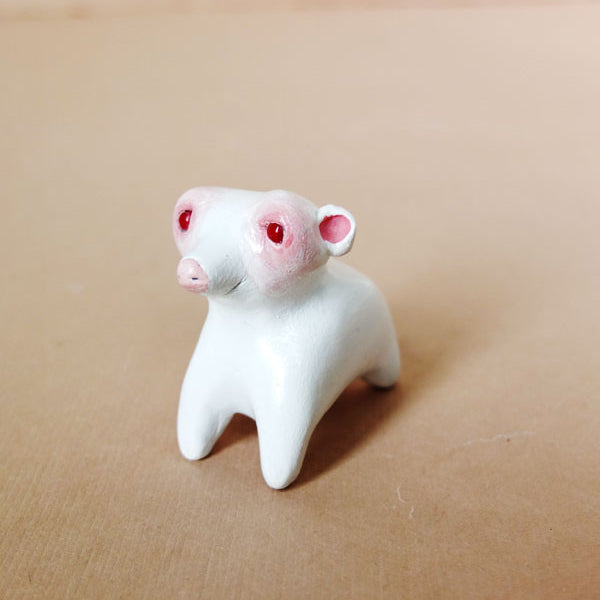 A small resin sculpture by Doubleparlour portrays a whimsical animal featuring pink ears, red eyes, and a pink nose, elegantly posed on a brown base.