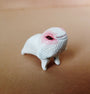 This hand-sculpted resin figure by Doubleparlour is a small, white creature with a textured surface, standing on four legs. It has a rounded body with a face featuring a pink patch and one dark eye against a light brown backdrop.
