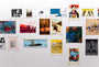 A gallery wall displays Joel Phillips posters and artworks, featuring film-themed pieces with diverse styles. Custom framing and UV-resistant plexiglass preserve the mix of portraits, abstract designs, and scenes on a pristine white wall.