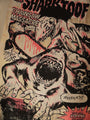 A comic-style image from Shark Toof Chainsaw Massacre shows a shark wielding a chainsaw confronting a scared person with dramatic text like JESSICA?! and WHO WILL SURVIVE AND WHAT. This striking print is in black, pink, and white.