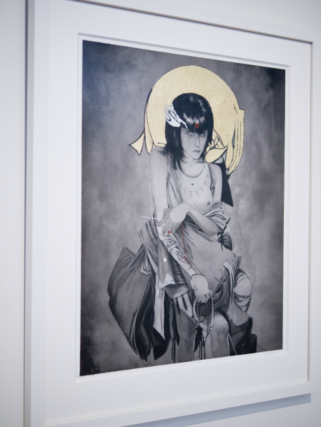 A framed artwork by Nimit Malavia shows a solemn person with long hair, wearing intricate clothing and jewelry. A metallic gold halo highlights their head, crafted in black, white, and gold.