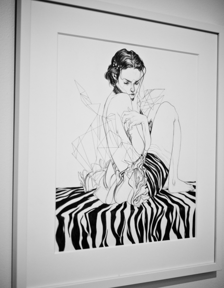 A black and white drawing by Nimit Malavia features a seated person with geometric shapes, set against a zebra-striped background. Its crafted with graphite on paper and elegantly framed for display at Spoke Art Gallery.