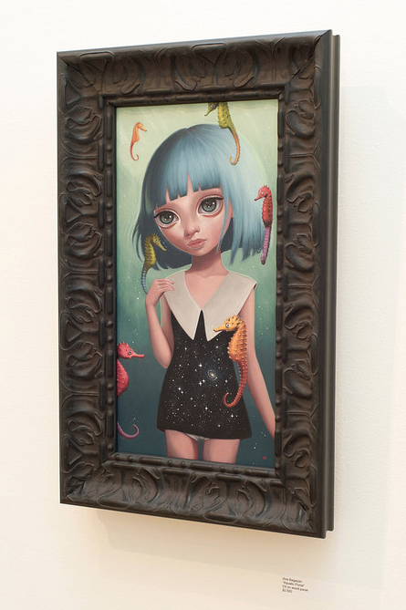 An Ana Bagayan framed oil on wood painting portrays a blue-haired, large-eyed girl in a black dress with a white collar. She is surrounded by colorful seahorses forming an aquatic portal, set against a green background. The piece is encased in an ornate black frame with intricate patterns.