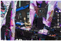 A vibrant abstract collage on canvas by Derek Gores showcases layers of torn paper with text, patterns, and mixed textures. Dominated by purple, black, and white tones, the artwork creates a dynamic and chaotic visual composition perfect for any art gallery.