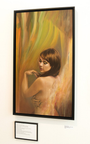 Nathan DeYoungs Sheltered Layers features a framed acrylic painting of a woman with short brown hair, gazing downward with crossed arms. The background shows soft shades of green, orange, and yellow. Displayed on a white wall with a plaque beneath it.