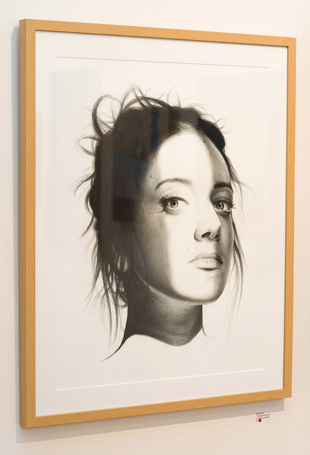 This captivating portrait, styled like Matt Doust, showcases a woman with loose hair in a contemplative side pose. The graphite on paper piece is intricately detailed and elegantly set within a light wooden frame, giving it an intriguing floating exposure effect.