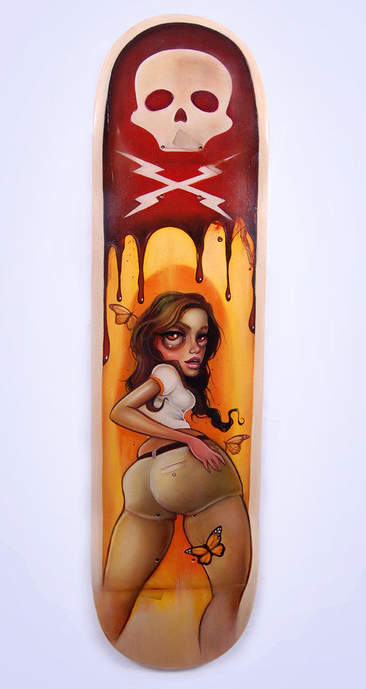 The Tatiana Suarez skateboard deck showcases stunning surreal art: a long-haired woman with a butterfly on her leg looks over her shoulder, while a melting skull floats above against a reddish-brown background, evoking vivid imagination akin to an art gallery piece.