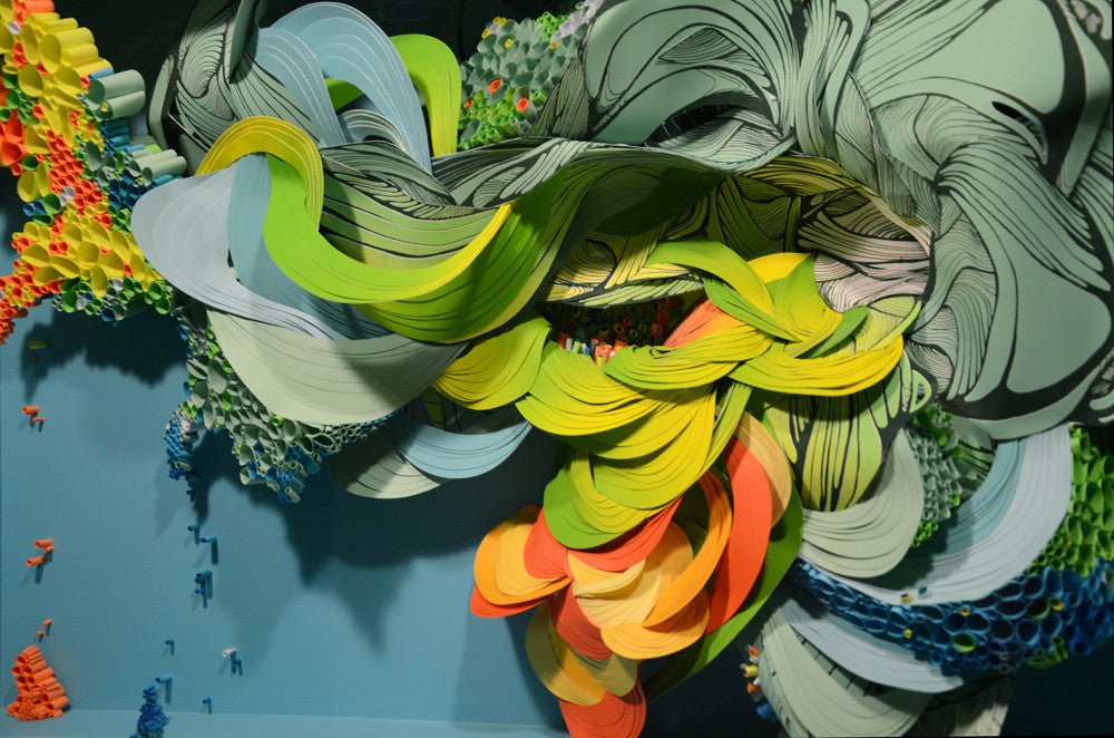 Crystal Wagners vibrant abstract installation, similar to Terrarium VI, showcases swirling green, yellow, and orange cut paper ribbons with blue, red, and green accents against a teal backdrop for a dynamic scene.