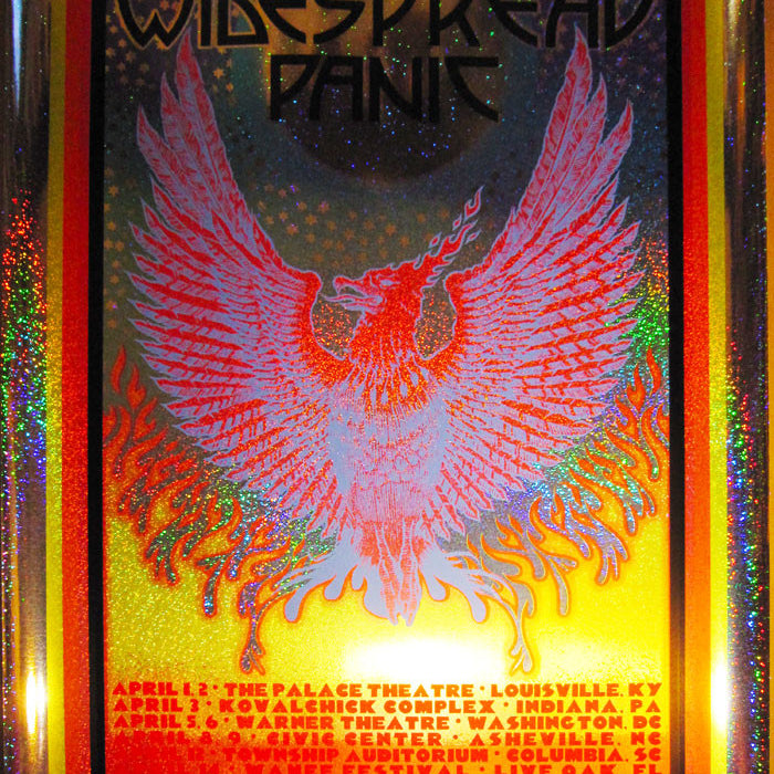 A vibrant concert poster by Chuck Sperry features a phoenix illustration and sparkle holographic foil. It reads 25th Anniversary Tour, Widespread Panic with venue details below, all set against a metallic, colorful background that completes this anniversary tour masterpiece.