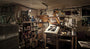 A dimly lit art studio displays the creative world of New Flesh. Shelves hold paint cans and supplies, while a screen printing station crafts intricate pieces with metallic inks. Signed and numbered posters and artworks by New Flesh enhance the vibrant atmosphere.