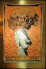 A Chuck Sperry psychedelic concert poster features a stylized silhouette with flowing hair against a vibrant, intricate background. Brushed gold foil accents highlight the text at the bottom announcing Widespread Panic and concert details, echoing Sperrys iconic style.